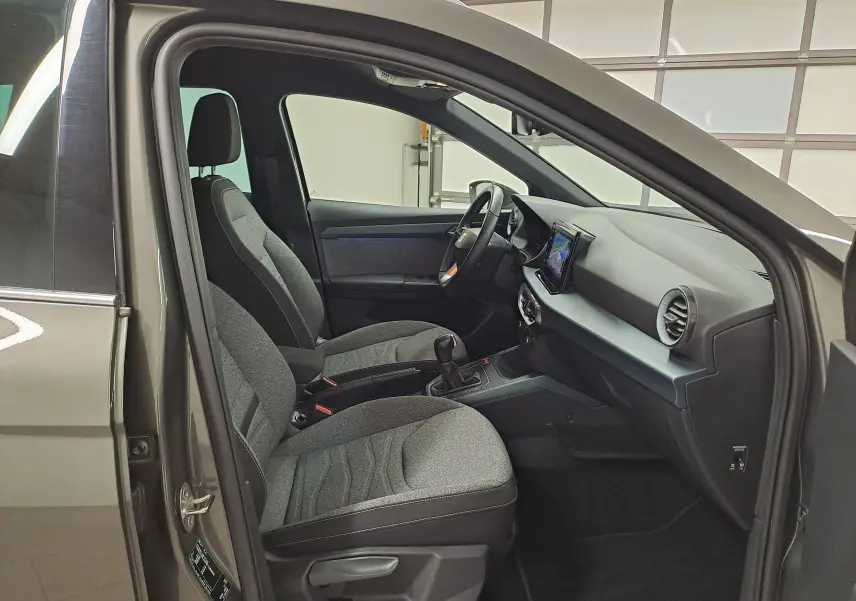 Vue intérieure côté conducteur du SEAT Arona gris falaise 2024, montrant sièges tissu et tableau de bord moderne.