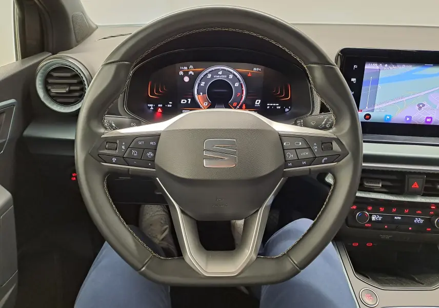 Vue intérieure centrée sur le volant multifonction du SEAT ARONA 2024 avec tableau de bord numérique et écran tactile.