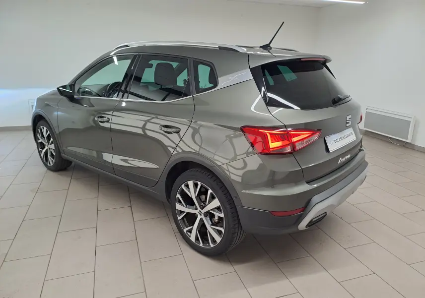 SEAT Arona gris falaise vue 3/4 arrière droit, jantes alliage 18'' et vitres arrière surteintées en intérieur showroom.