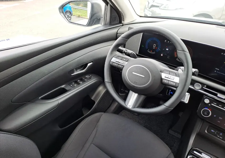 Intérieur noir du Hyundai Tucson 2025, vue côté conducteur sur le volant et tableau de bord numérique moderne.