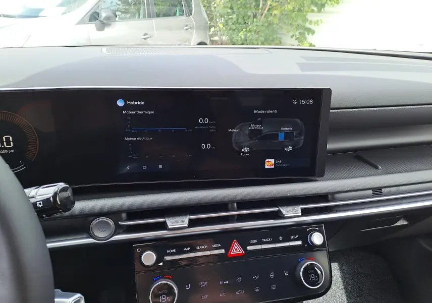 Vue intérieure du tableau de bord du Hyundai Tucson 2025 gris, écran tactile affichant les données hybrides et commandes climatisation.