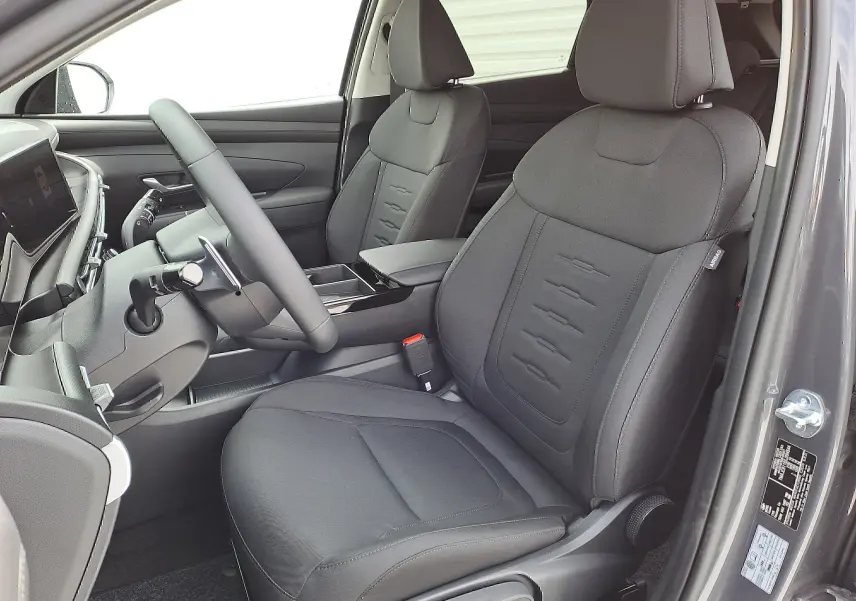 Vue intérieure côté conducteur du Hyundai Tucson 2025 gris Ecotronic, sièges tissu noir avec détails cousus et tableau de bord moderne.