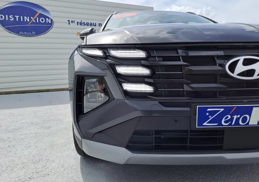 Vue rapprochée avant gauche du Hyundai Tucson 2025 gris Ecotronic avec feux LED distinctifs et calandre noire.