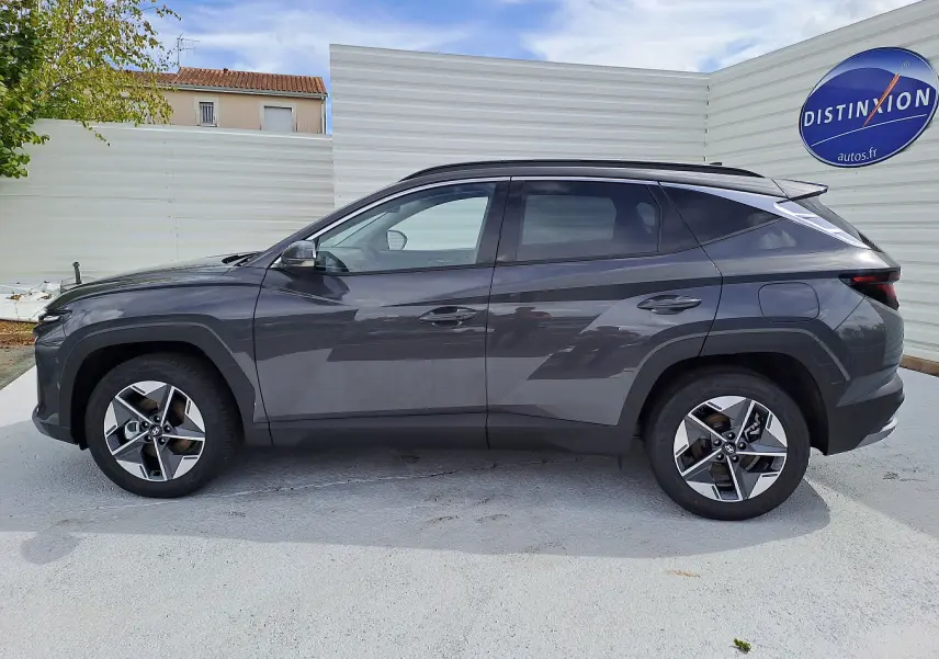 Profil côté gauche du Hyundai Tucson 2025 hybride en gris Ecotronic, avec jantes alliage et toit noir contrasté visible.