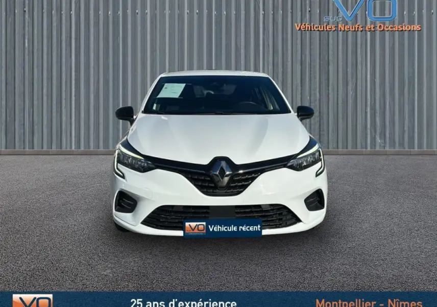 Vue frontale d'une Renault Clio blanche 2021 avec calandre noire et phares LED allumés sur fond urbain.
