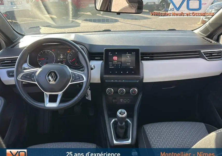 Vue intérieure avant de la Renault Clio blanc, tableau de bord moderne avec écran tactile et volant multifonction.