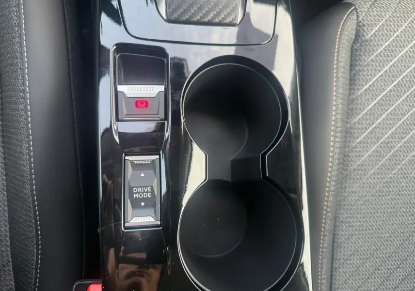 Vue rapprochée de la console centrale noire avec boutons Drive Mode et frein à main électrique sur Peugeot 208 gris.