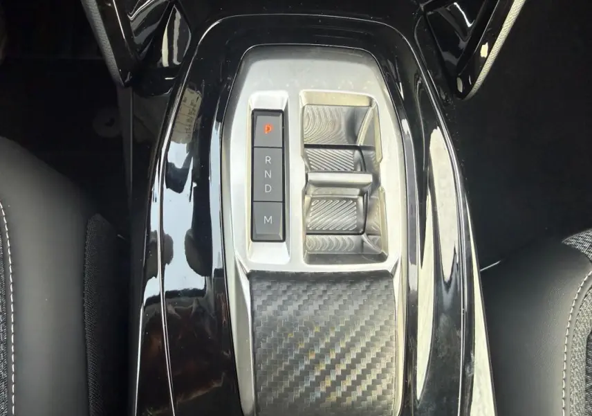 Gros plan sur la console centrale noire brillante de la Peugeot 208 Hybrid 110 e-DCS6 Allure avec sélecteur de boîte auto.