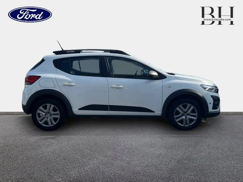 Profil droit d'une Dacia Sandero blanche 2023 avec barres de toit et jantes alliage 16 pouces Mahalia.