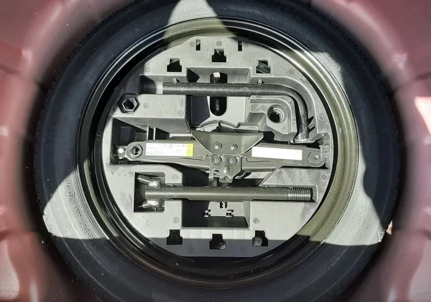Vue plongeante sur la roue de secours et les outils de bord dans le coffre rouge flamme d'une Renault Clio V 2024.