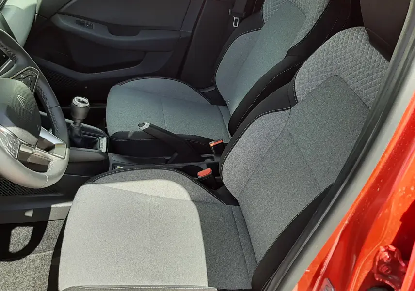 Vue intérieure côté conducteur de la Renault Clio V rouge flamme, montrant les sièges tissu gris et la boîte manuelle.