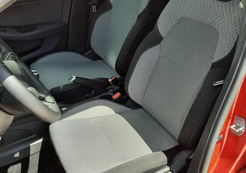 Vue intérieure côté conducteur de la Renault Clio V rouge flamme, mettant en valeur les sièges tissu gris et la console centrale.