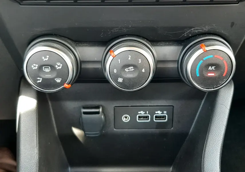 Vue rapprochée des commandes de climatisation et des ports USB du tableau de bord de la Renault Clio V rouge flamme 2024.