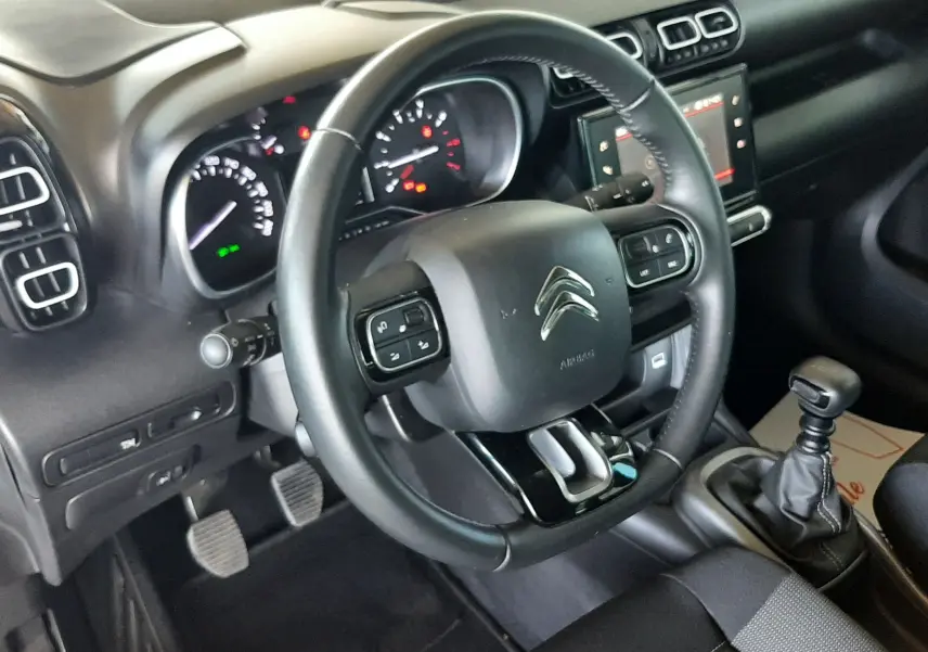 Intérieur noir de la Citroën C3 Aircross 2021, vue côté conducteur sur volant, tableau de bord et levier de vitesse manuel.