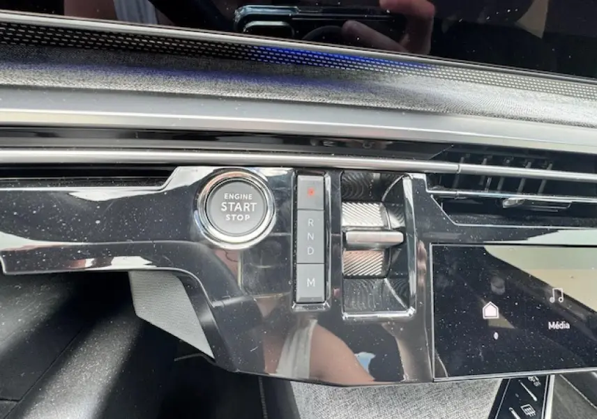 Gros plan sur la console centrale noire brillante du Peugeot 5008 2024 avec bouton start/stop et levier de boîte automatique.