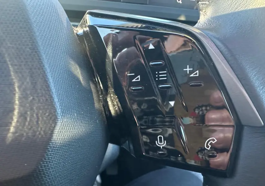 Gros plan sur les commandes au volant noir brillant du Peugeot 3008 Hybrid blanc, côté gauche, avec boutons multifonctions.