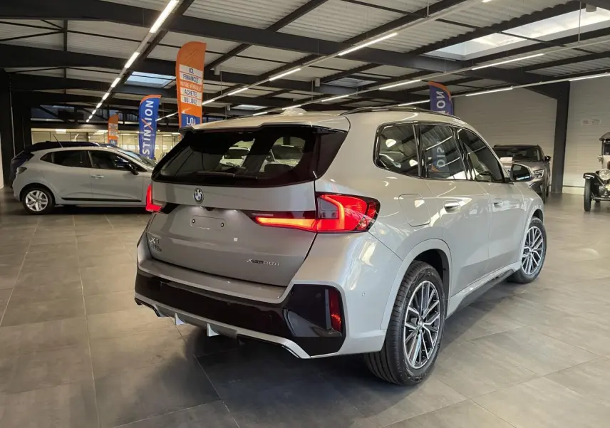 BMW X1 xDrive 20d 2024 en Spacesilber Metallic, vue 3/4 arrière droite avec feux arrière LED allumés.