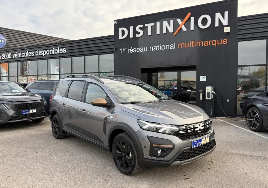 Vue 3/4 avant du Dacia Jogger gris schiste métal avec calandre noire et jantes aluminium noires devant un showroom Distinxion.