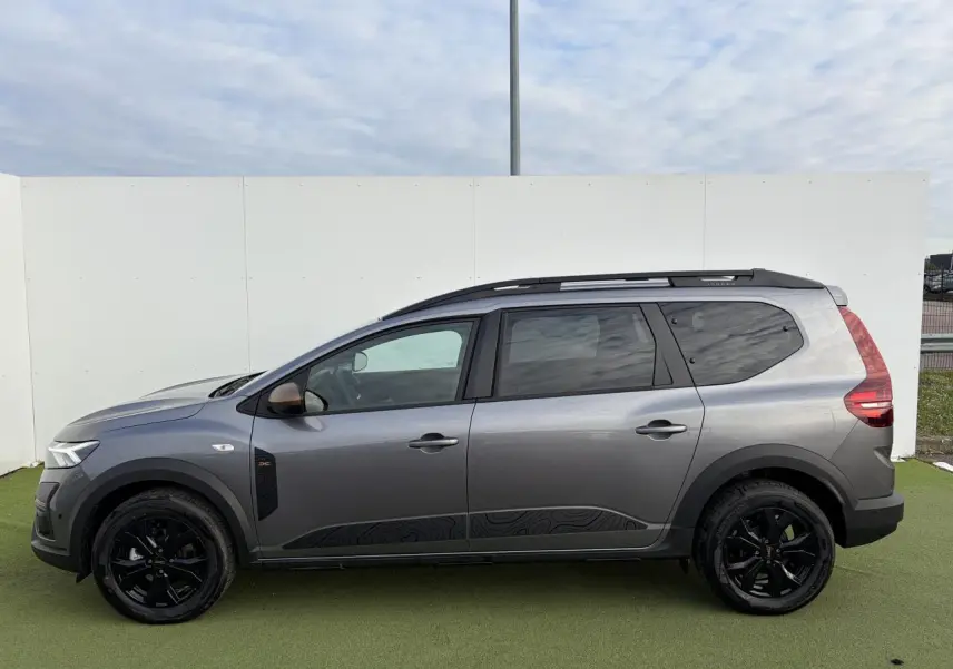 Profil côté gauche d'un Dacia Jogger gris schiste métal avec jantes noires et barres de toit modulaires.