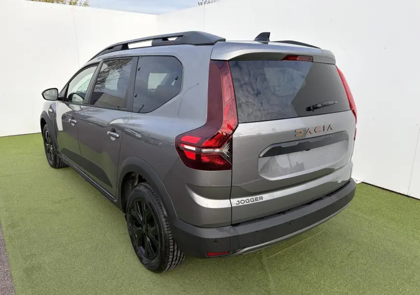 Vue 3/4 arrière droite d'un Dacia Jogger gris schiste métal avec barres de toit noires et jantes noires.