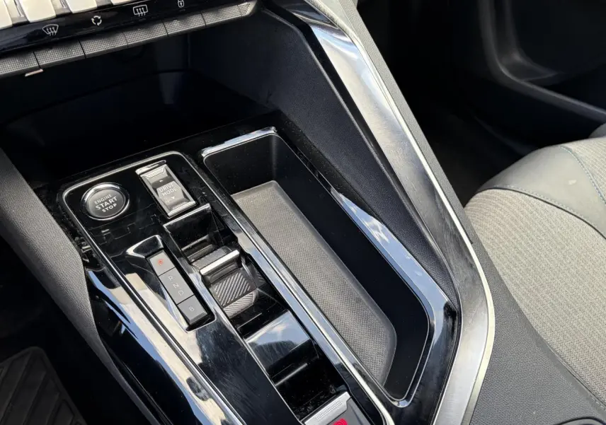 Gros plan sur la console centrale noire brillante du Peugeot 3008 Plug-in Hybrid 2024 avec sélecteur de vitesses et bouton start/stop.