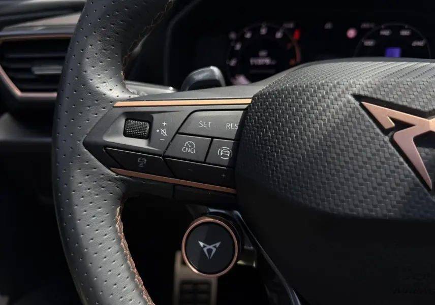 Gros plan sur le volant perforé noir avec logo CUPRA cuivré et commandes multifonctions à gauche, intérieur du Formentor 2025.