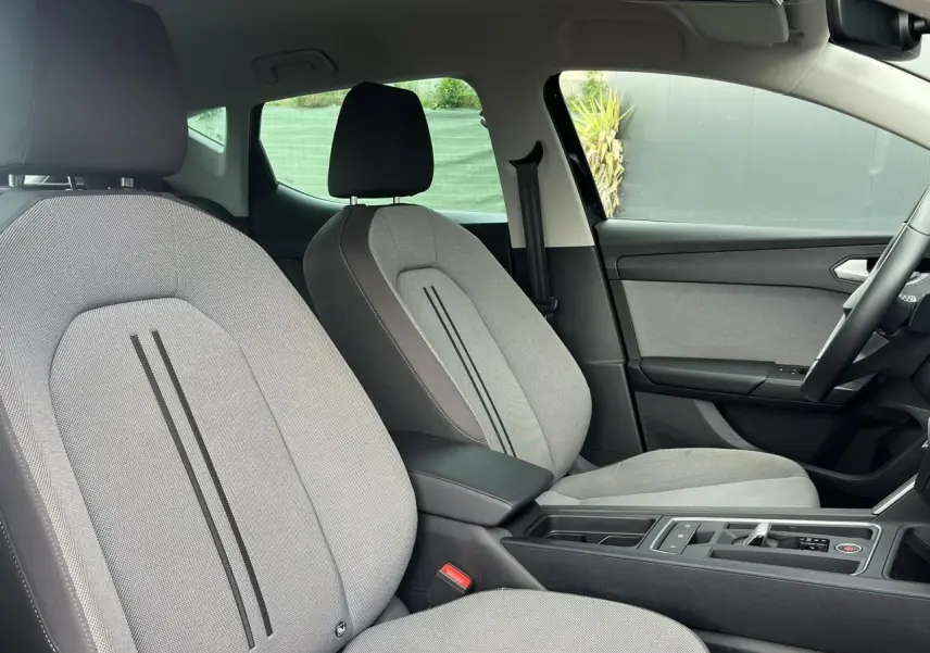 Intérieur de la SEAT LEON 2024 vu côté droit, sièges tissu gris clair avec accoudoir central noir.