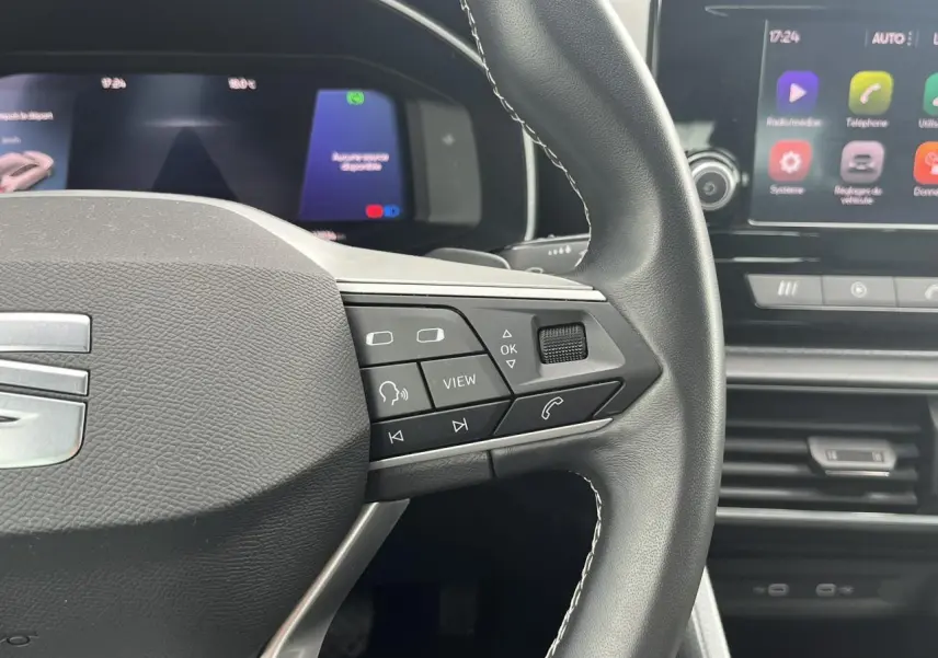 Gros plan sur le volant cuir multifonction de la SEAT LEON 2024, avec commandes intégrées et écran digital en arrière-plan.