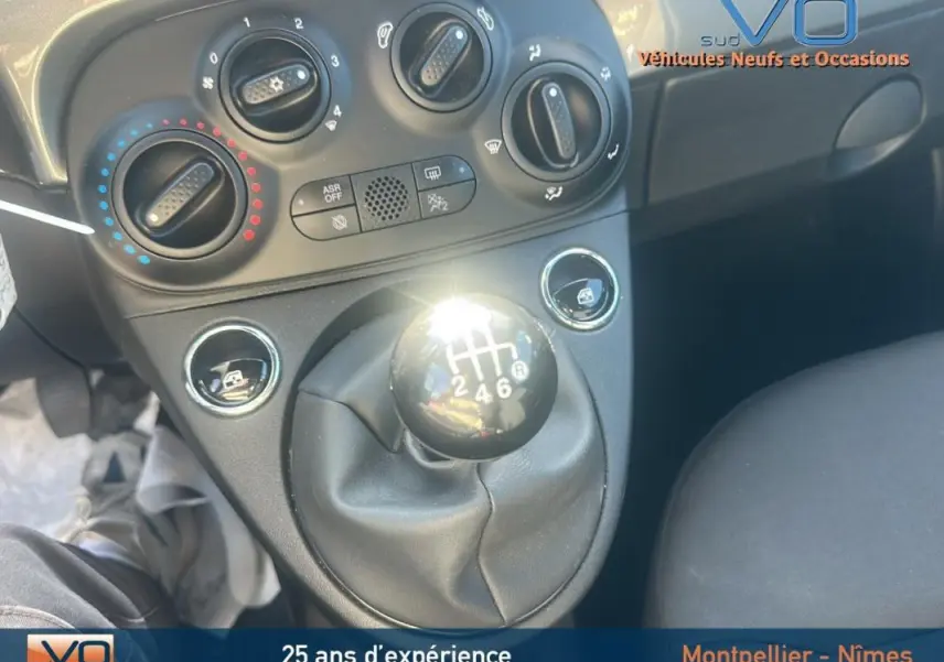 Gros plan sur la commande de boîte manuelle noire et les réglages climatiques du tableau de bord d'une Fiat 500 gris 2023.