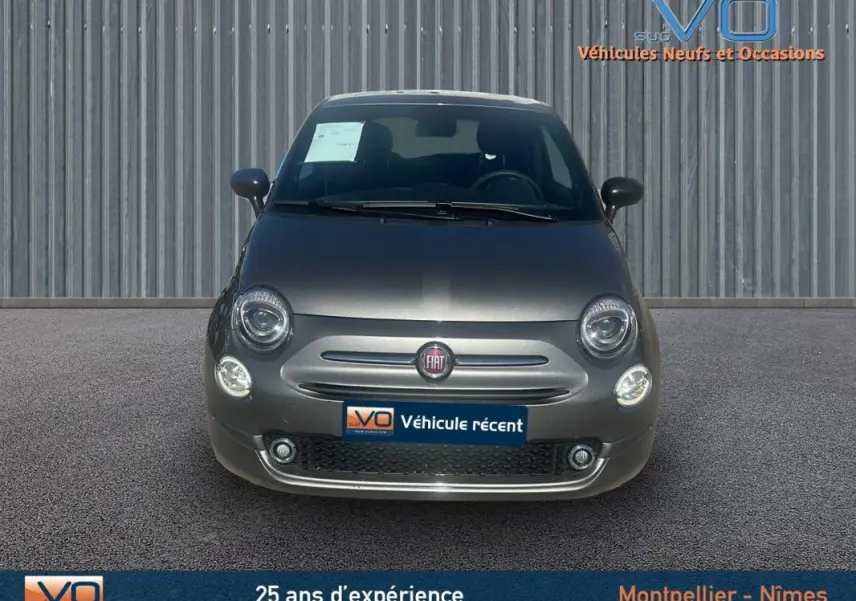 Vue avant d'une FIAT 500 gris métallisé 2023 avec phares ronds et logo central sur fond urbain.