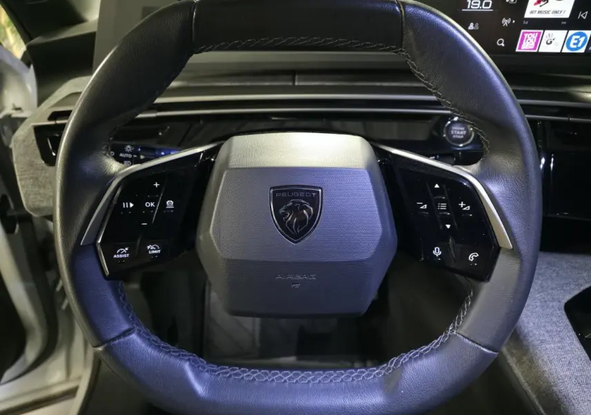 Volant compact cuir noir avec commandes intégrées et logo Peugeot au centre, vue frontale intérieure du 3008 hybride 2025.