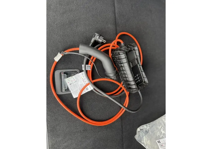 Câble de recharge orange et noir posé sur le tapis du coffre d’un Peugeot 3008 Plug-in Hybrid noir Perla.