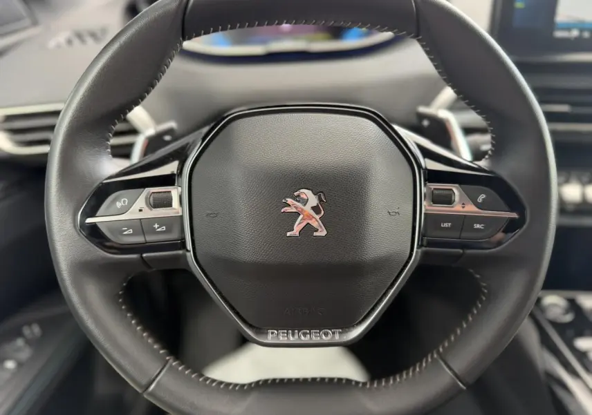 Volant cuir noir Mistral au design compact avec logo Peugeot, vue rapprochée centrée sur les commandes intégrées.