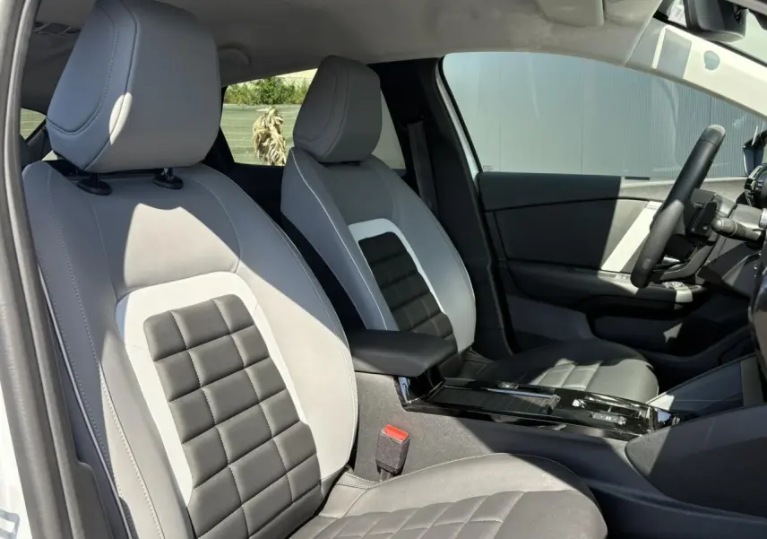 Vue intérieure côté conducteur de la Citroën C4 Hybrid 2025 avec sièges bicolores gris clair et noir, et console centrale brillante noire.