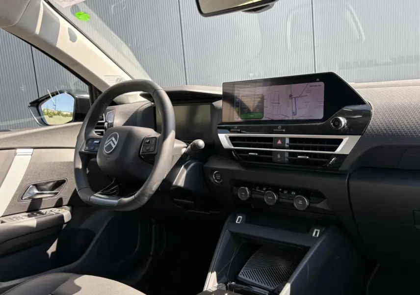 Vue intérieure côté conducteur de la Citroën C4 Hybrid blanche avec tableau de bord moderne et écran tactile GPS.