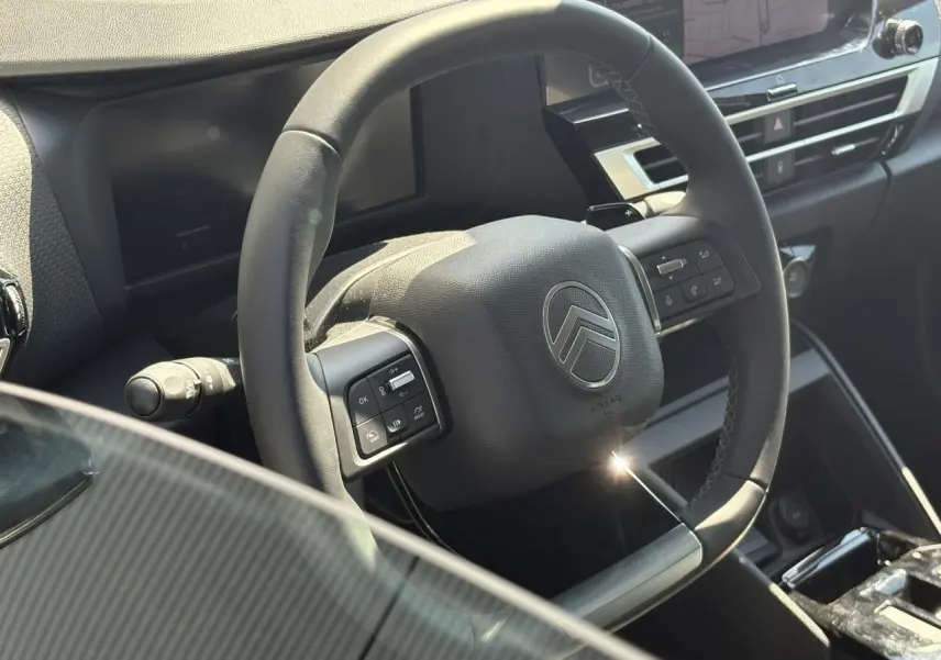 Vue rapprochée du volant cuir noir de la Citroën C4 Hybrid 2025 avec commandes intégrées et tableau de bord moderne.