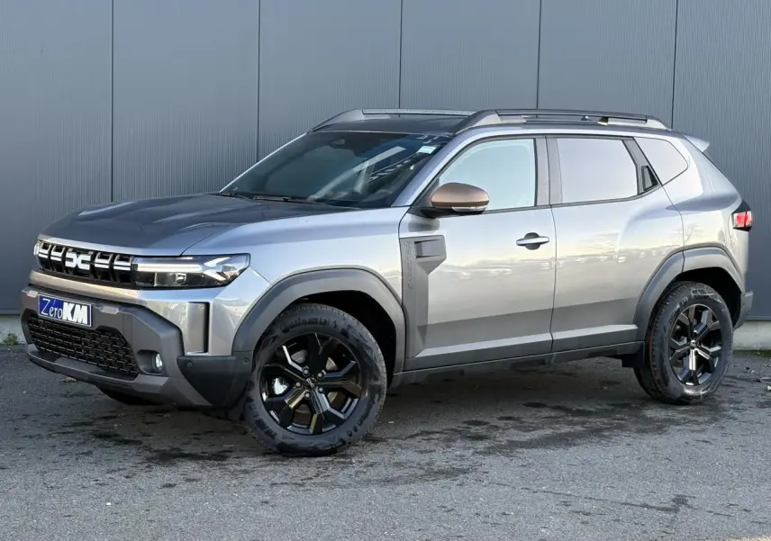 Vue 3/4 avant droit du Dacia Duster 2026 gris schiste avec jantes noires et barres de toit longitudinales.