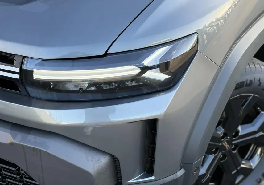 Gros plan sur le phare avant gauche et la roue alliage noire du Dacia Duster gris Schiste 2026.