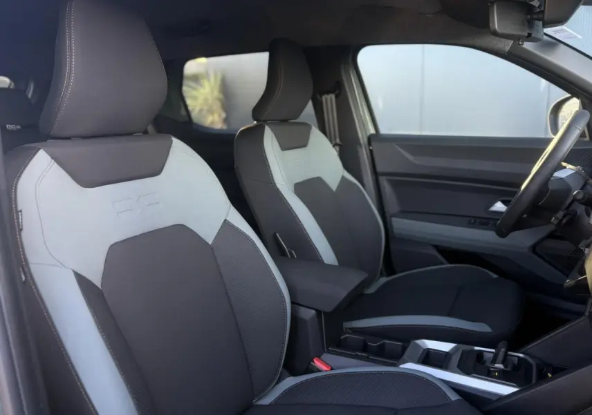 Vue intérieure côté conducteur du Dacia Duster 2026, sièges TEP MicroCloud gris clair et foncé avec accoudoir central.