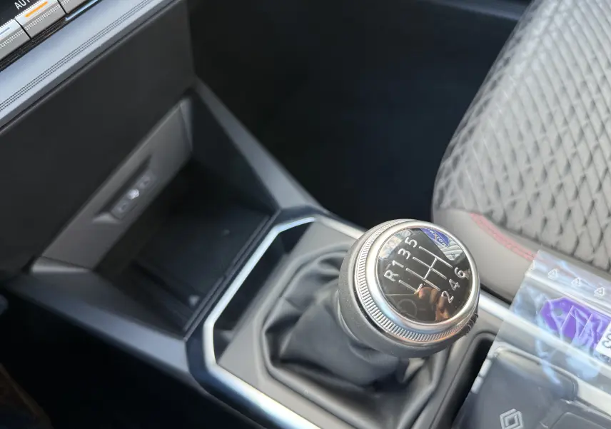 Gros plan sur le levier de vitesses manuel de la Renault Clio VI TCe 115 Techno, intérieur gris avec surpiqûres rouges.