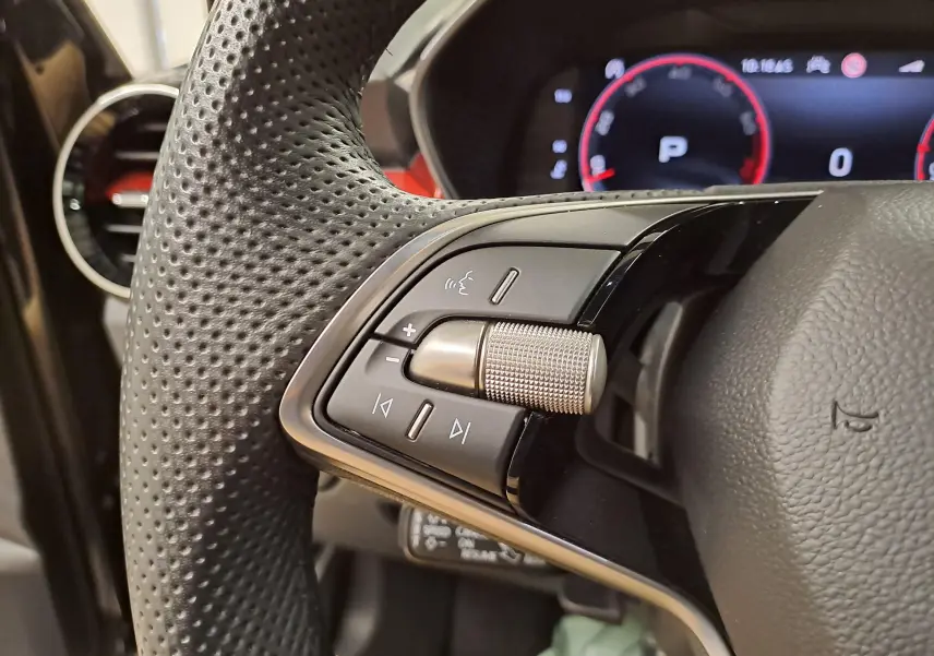 Gros plan sur les commandes gauche du volant perforé d'une Skoda Fabia 1.5 TSI 2024 avec tableau de bord numérique en arrière-plan.