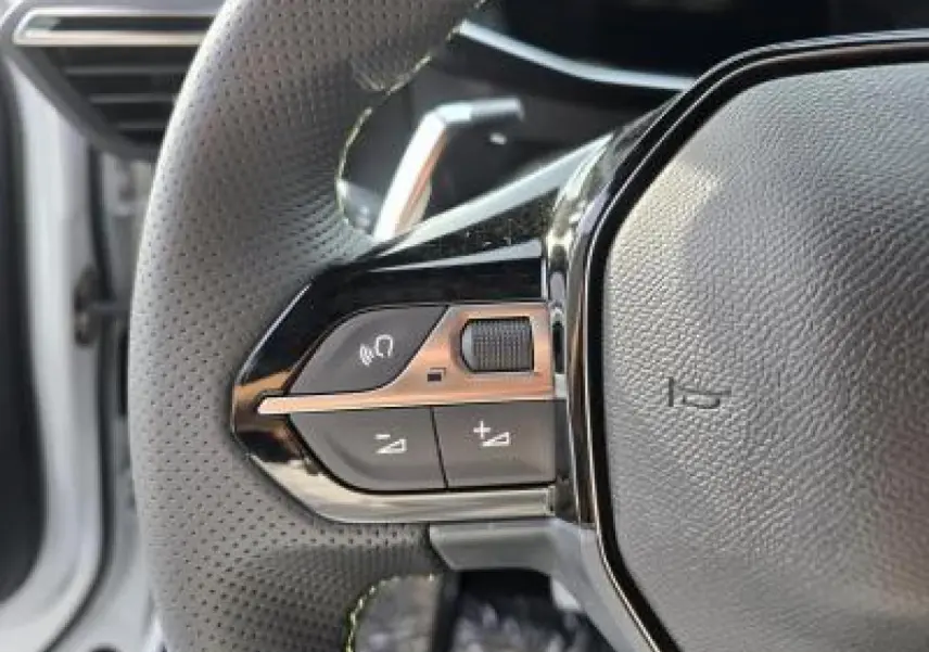 Gros plan sur le volant cuir noir avec logo Peugeot et badge GT du Peugeot 2008 hybride blanc, intérieur moderne.