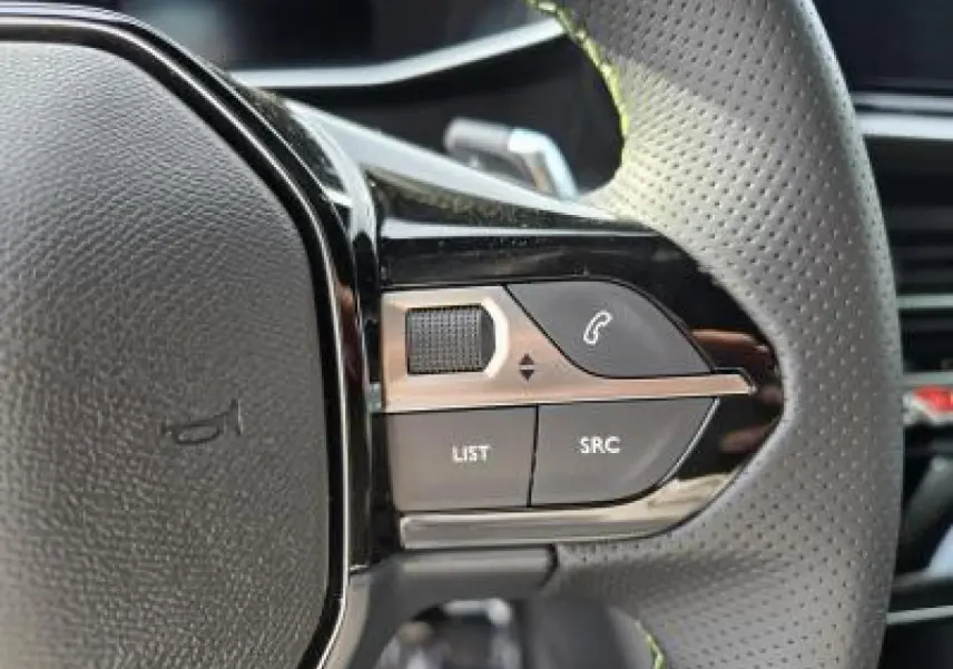 Gros plan sur les commandes gauche du volant cuir perforé de la Peugeot 2008 blanche toit noir, version hybride 2025.