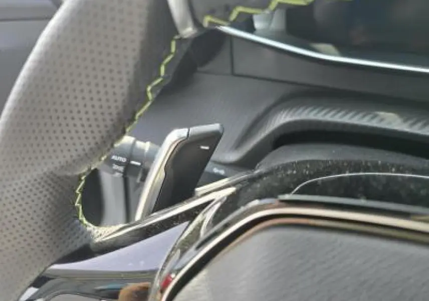 Gros plan sur les commandes gauche du volant cuir perforé du Peugeot 2008 blanc Okenite, version hybride 2025.