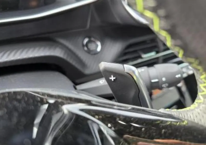 Gros plan sur le volant cuir perforé avec surpiqûres vertes et palettes de changement de vitesse du Peugeot 2008 hybride 2025.