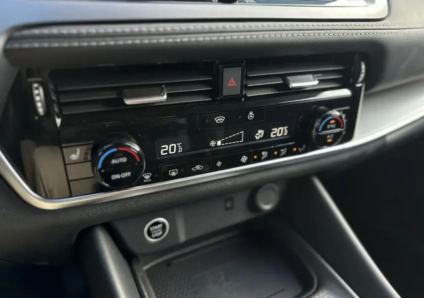 Vue rapprochée de la console centrale noire du Nissan Qashqai 2025, mettant en valeur la climatisation automatique bi-zone et le bouton Start/Stop.