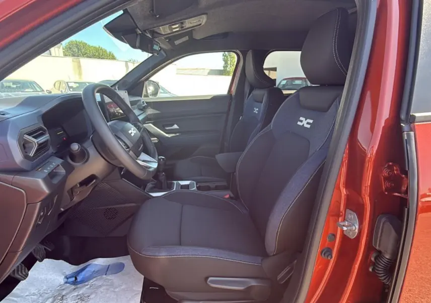 Vue intérieure côté conducteur du Dacia Duster orange 2025, montrant les sièges et le volant réglable.
