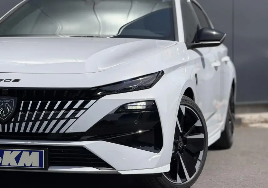 Vue avant droite d'une Peugeot 308 blanche Okenite avec calandre noire et jantes alliage 18" bi-tons.
