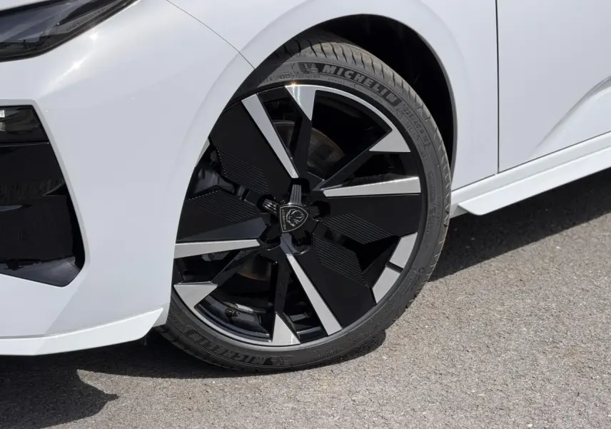 Gros plan sur la roue avant droite noire et argentée de la Peugeot 308 NV Hybrid 145 GT blanc Okenite.