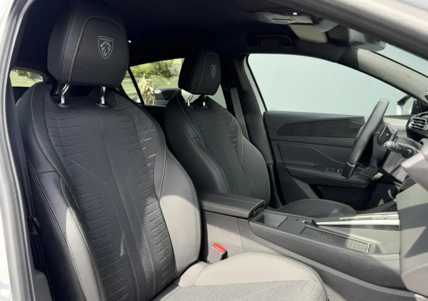 Vue intérieure côté conducteur de la Peugeot 308 NV Hybrid 145 GT avec sièges noirs embossés et volant cuir.